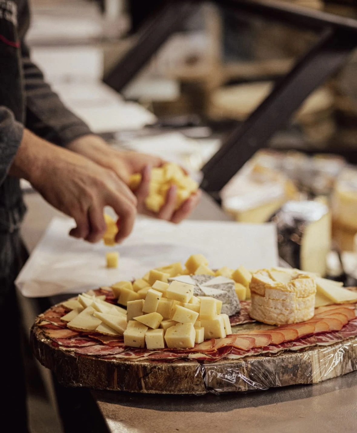 Une image d'un plateau de charcuterie, avec une main qui dépose une tranche de fromage dessus.