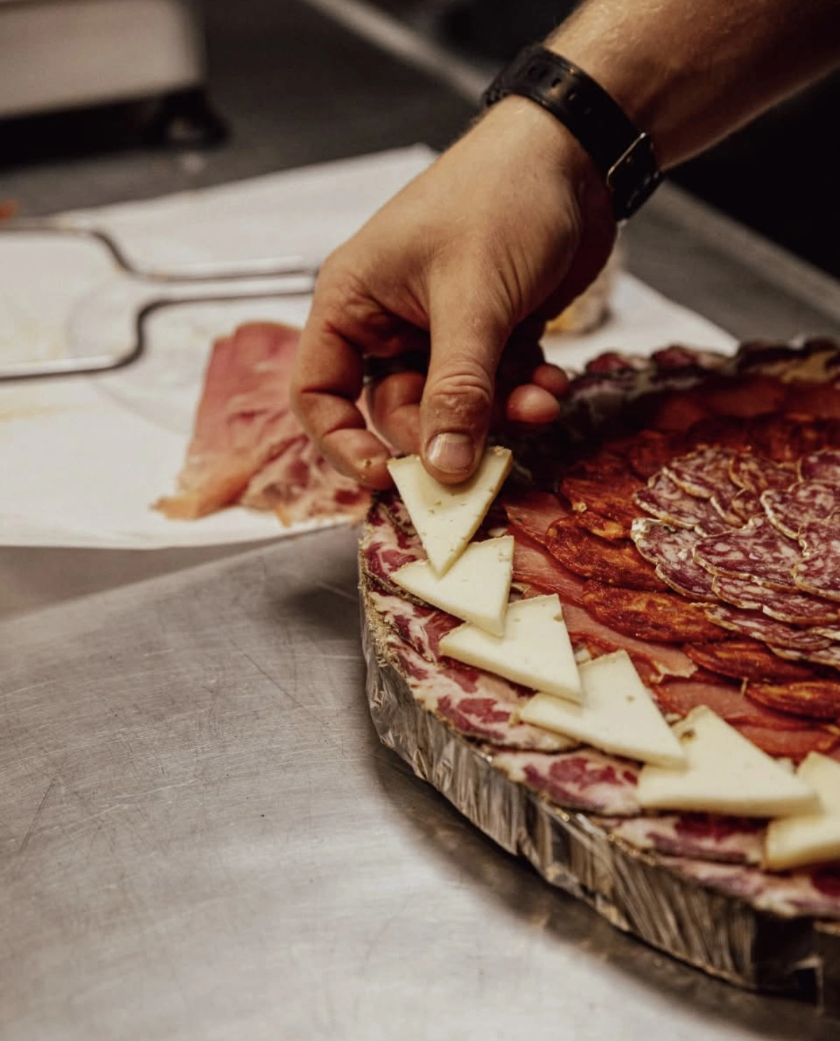 Une image d'un plateau de charcuterie, avec une main qui dépose une tranche de fromage dessus.