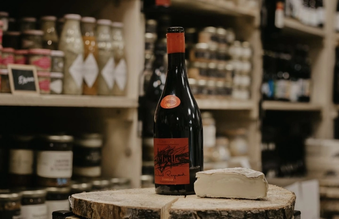 une image d'une bouteille de vin rouge et d'un fromage sur un plateau en bois.