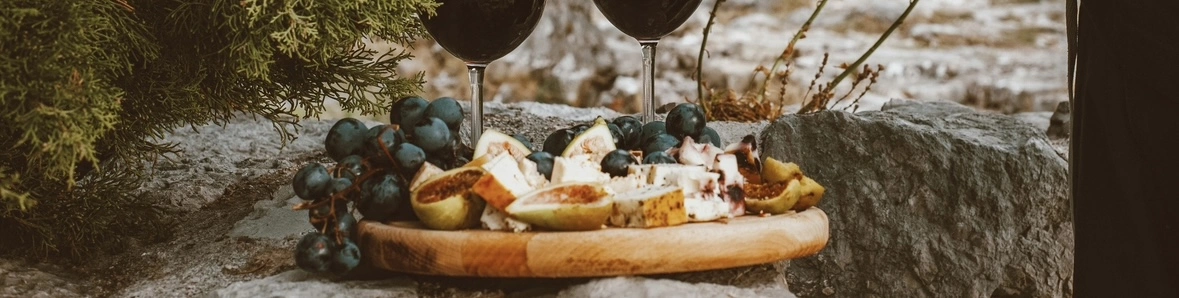 Une image de plateau de fromage, avec deux verres de vin rouge à cotés.