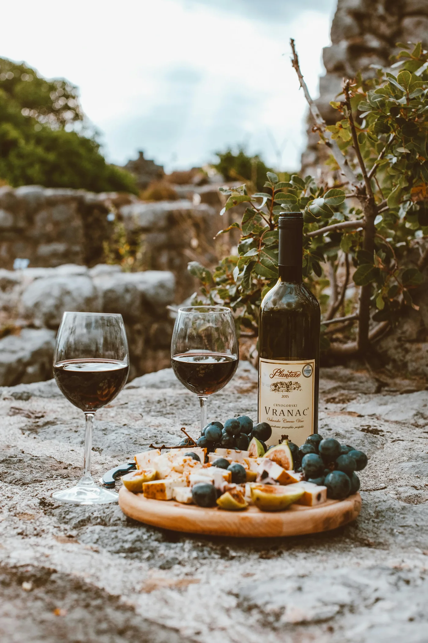 Une image d'une bouteille de vin rouge, avec deux verres de vin et un plateau de fromage et du raisin à coté.
